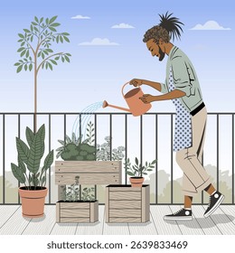 A young man is watering plants on a balcony using a watering can. There are wooden planters with various herbs and flowers around him. A large potted plant stands nearby. 