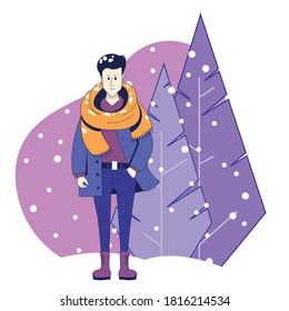 A young man in winter clothes stands under the falling snow against the background of Christmas trees.