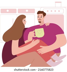 The young man and the young woman drink tea in the kitchen, sitting on the floor and hugging.
