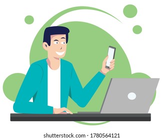 Young man working from home with laptop sitting at the desk holding phone.