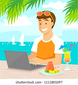 Young man working on his laptop at the beach while enjoying tropical fruit and a cocktail.