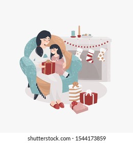 young mother and daughter sit in a chair by the fireplace and open Christmas presents