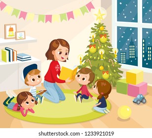 Young mother teacher nurse babysitter reading fairytale book to children kids pupils at Christmas tree on Christmas Eve,New year.Children in kindergarden,primary school,pre-school,listen to teacher.