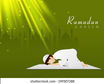 Young Muslim boy praying in shiny night on mosque silhouetted background for holy month of Ramadan Kareem. 