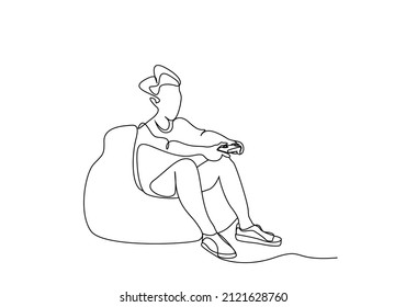 a young person sitting on a pear puff sofa plays with a console in his hand with his full body visibly