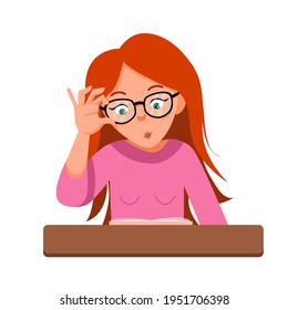 A young schoolgirl with glasses is sitting at a desk. The girl does her homework, reads a book.