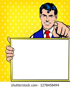 Young Smiling Business man pointing finger at you and holding empty, blank white borad, sign or paper sheet. Vector illustration in Comic Book Pop Art retro vintage style