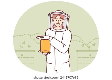 Young woman beekeeper in protective uniform holding jar of honey standing in apiary among flying bees. Girl farmer breeds bees in garden getting organic honey for sale at fair of ecological products