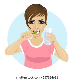 young woman brushing teeth and holding glass of water
