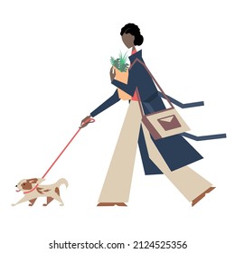 A young woman in a coat walks with a dog along the street and carries a bag of greens in her hands