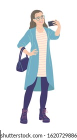 Young woman with glasses taking selfie photo on smartphone. Bespectacled girl in cardigan and boots holding mobile phone isolated on white. Simple female character in flat style vector illustration.