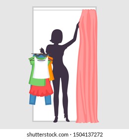 Young woman is holding many different clothes on hangers in one hand and pulling curtain in fitting room with another hand. Slender silhouette. Modern female shopping and difficulties of choices