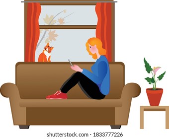 Young woman holding smartphone sits on sofa and surfing internet  near the window with a ginger cat in autumn.