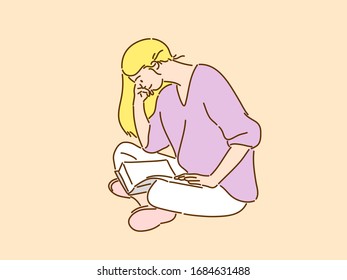 A young woman with long hair is sitting comfortably and looking at a book.