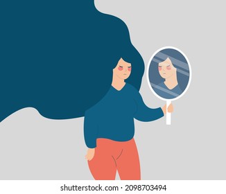 Young woman looks on her reflection in the mirror in a sad way. Girl holding a mirror and looks upset. Mental health illness, depression, stress, lack of confidence, Body Dysmorphic Disorder concept.