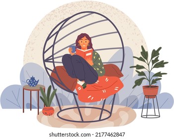 Young woman reading book, sitting on pillows in modern chair. Leisure and education. Relaxation with literature. Girl relaxing at home and drinking coffee. Student reads textbook holds cup in hand