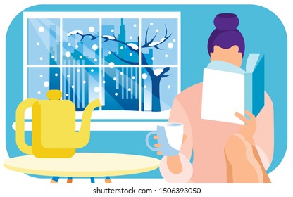 Young Woman Reading Interesting Book, Having Some Tea On Her Cozy Home Kitchen. Large Window With Snowy Winter In Big City With Skyscrapers, Office Buildings And Bare Tree Outside. Good To Be At Home.