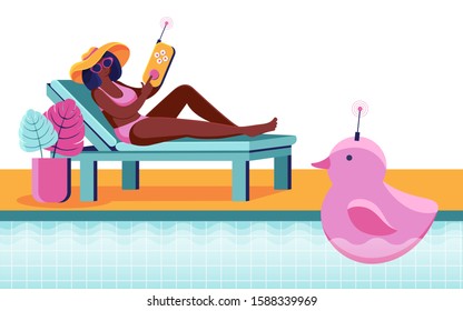 A young woman is relaxing on a sun lounger next to the pool and playing with a radio-controlled toy. Toy for swimming pool with remote control. Pink rubber duck in the pool. Summertime. Swimming toy