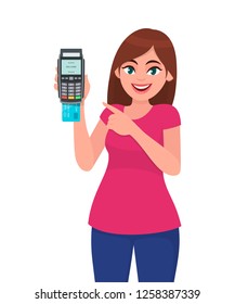 Young woman showing/holding pos payment terminal or credit/debit cards swiping machine and pointing finger. Wireless modern bank payment, business and finance concept illustration in vector cartoon.