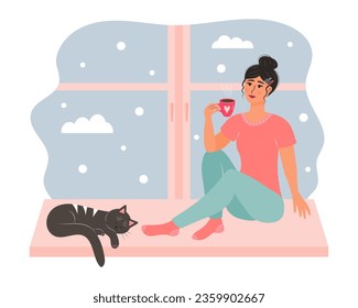 Young woman sitting on the window with a mug of hot drink and cute cat sleeping near her. Snowy day weather outside the window. 