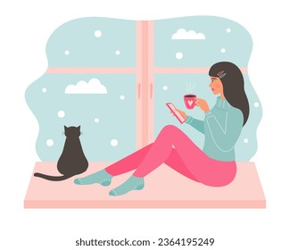 Young woman sitting on the window with a mug of hot drink and using smartphone. Black cat sitting and looking out the window. Snowy day weather outside the window.