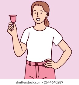 Jovem mulher fica com a mão no quadril e segura confiantemente o copo menstrual. Conceito de higiene moderna e solução de período sustentável