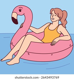 Young woman in swimsuit relaxes on inflatable pink flamingo in pool enjoying summer vacation and sunny weather