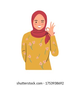 Young woman winking, smiling, and making OK sign with hand gesture.  Pretty lady wear hijab.