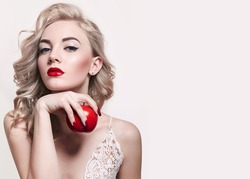 a blonde haired woman with red lipstick holds a bright red apple