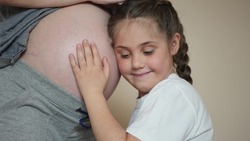 a little girl hugs her mother belly. happy family kid pregnancy newborn concept. the daughter sent her ear to the belly of dream the pregnant mother listens to the thrusts of the newborn brother