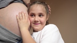 pregnant woman close-up belly. a little girl hugs her mother belly. happy family baby pregnancy newborn concept. daughter listening to pregnant mother belly. baby happy family expecting newborn