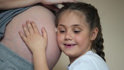 a little girl hugs her mother belly. happy family kid pregnancy dream newborn concept. the daughter sent her ear to the belly of the pregnant mother listens to the thrusts of the newborn brother