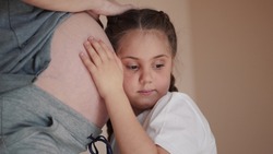 little girl hugs her mother belly. happy family kid pregnancy newborn concept. the daughter lifestyle sent her ear to the belly of the pregnant mother listens to the thrusts of dream the newborn
