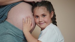 a little girl hugs her mother belly. happy family kid pregnancy newborn concept. the daughter sent her ear to the belly of the pregnant mother listens to dream the thrusts of the newborn brother