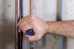 Man using strength to turn a water valve on a pipe gripping it with his hand indoors in a utility room in a close up view