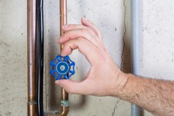 Male hand turning blue valve on copper pipe