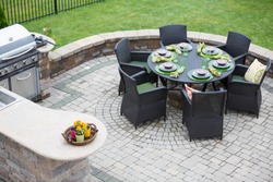 Elegant outdoor living space on a paved brick patio with a summer kitchen and barbecue and a table laid with formal place settings for dinner, high angle view