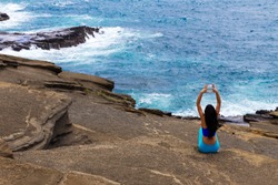 Young woman doing yoga exercises, Oahu, Hawaii as she sits on a rocky ledge overlooking the ocean at Heavens Point