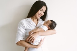 Beautiful young Asian mother and cute newborn son in her arms. Loving Asian mom hug embrace small baby child, relax enjoy tender family moment at home. Beautiful family, mother's day concept.