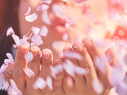 Woman blowing flower petals in her hands, close up