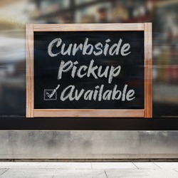 A business sign that says ‘Curbside Pickup Available’ on the window.