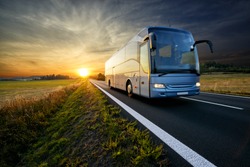 Bus traveling on the asphalt road in rural landscape at sunset                               