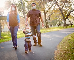 Happy Mixed Race Ethnic Family Walking In The Park Wearing Medical Face Mask.