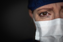 Tearful Stressed Female Doctor or Nurse Wearing Medical Face Mask on Dark Background.