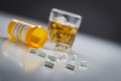 Several Prescription Drugs Spilled From Fallen Bottle Near Glass of Alcohol.