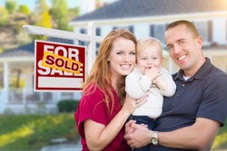 Happy Young Military Family in Front of Sold For Sale Real Estate Sign and New House.
