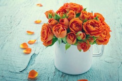 Vintage edited orange roses in a white cup on blue shabby chic wooden background