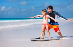 Father and daughter at beach practicing surfing position
