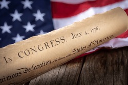 United States declaration of independence with American flag in background on rustic wooden table
