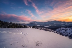 Beautiful sunrise view with snowy mountain slopes and small village among them in the frozen winter morning, the Rhodopi Mountains, Bulgaria 	